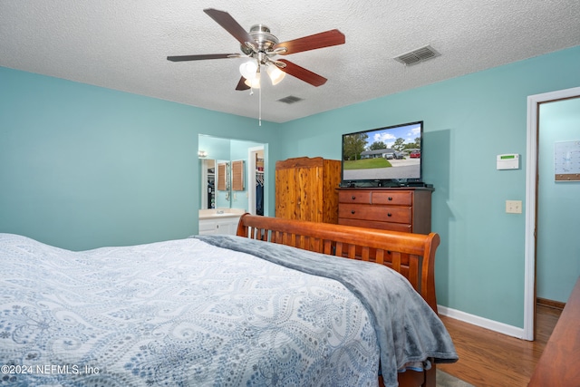 bedroom with a textured ceiling, hardwood / wood-style flooring, connected bathroom, and ceiling fan