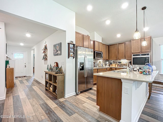 kitchen featuring sink, stainless steel appliances, vaulted ceiling, decorative light fixtures, and light hardwood / wood-style flooring