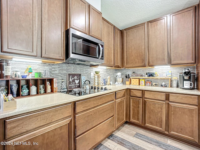 kitchen with black electric cooktop, light hardwood / wood-style flooring, light stone countertops, a textured ceiling, and tasteful backsplash