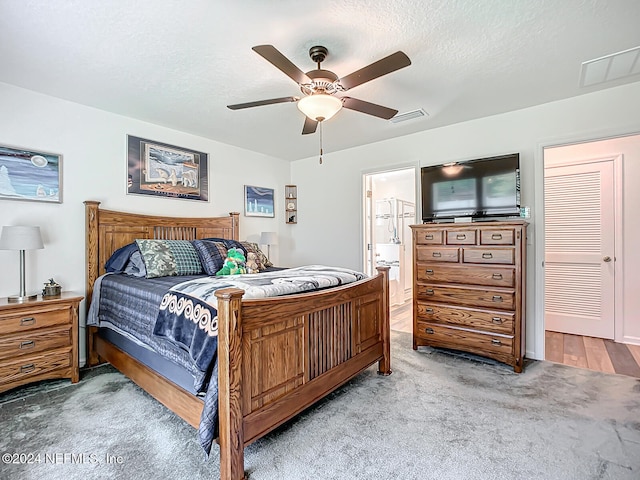 bedroom with ceiling fan, a textured ceiling, ensuite bathroom, and light colored carpet