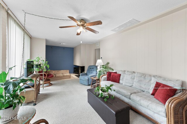 living room featuring a wood stove, carpet floors, a textured ceiling, and ceiling fan