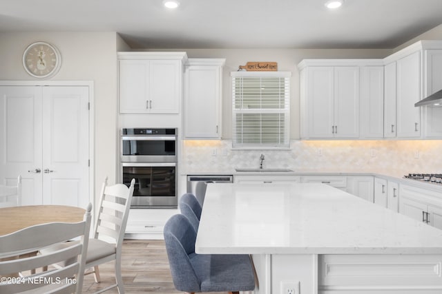 kitchen with white cabinetry, light wood-type flooring, appliances with stainless steel finishes, backsplash, and sink