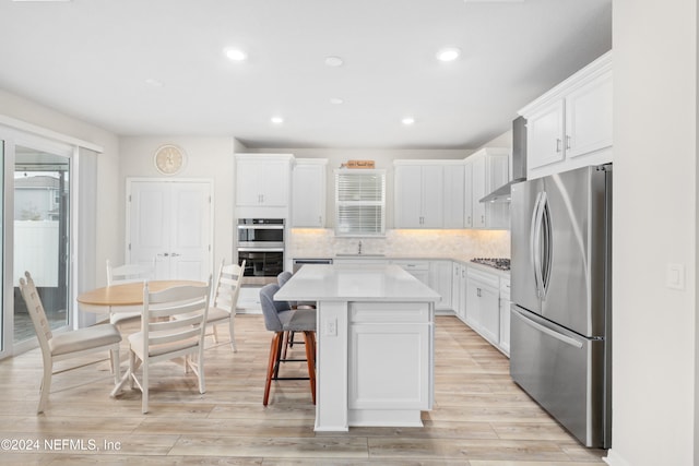 kitchen with white cabinets, decorative backsplash, a kitchen island, light wood-type flooring, and appliances with stainless steel finishes