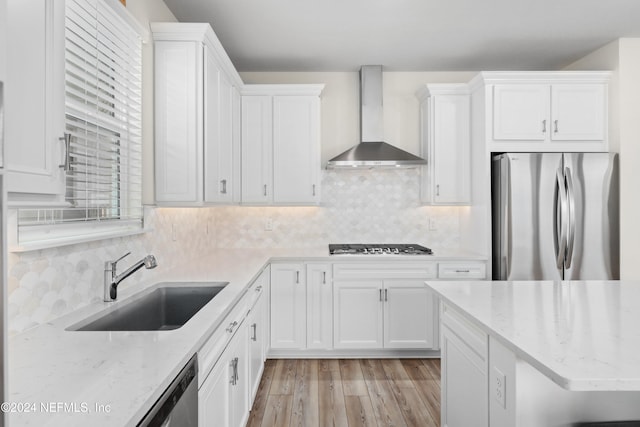 kitchen with light hardwood / wood-style floors, stainless steel appliances, white cabinets, wall chimney exhaust hood, and sink