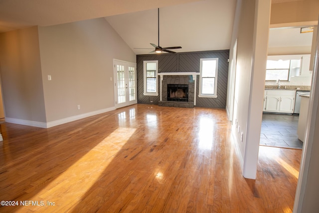 unfurnished living room featuring wood walls, a fireplace, light hardwood / wood-style floors, ceiling fan, and high vaulted ceiling