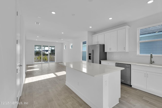 kitchen featuring sink, appliances with stainless steel finishes, tasteful backsplash, white cabinets, and a kitchen island