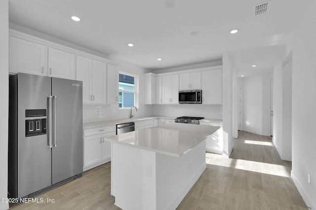 kitchen featuring stainless steel appliances, a center island, white cabinets, and light wood-type flooring