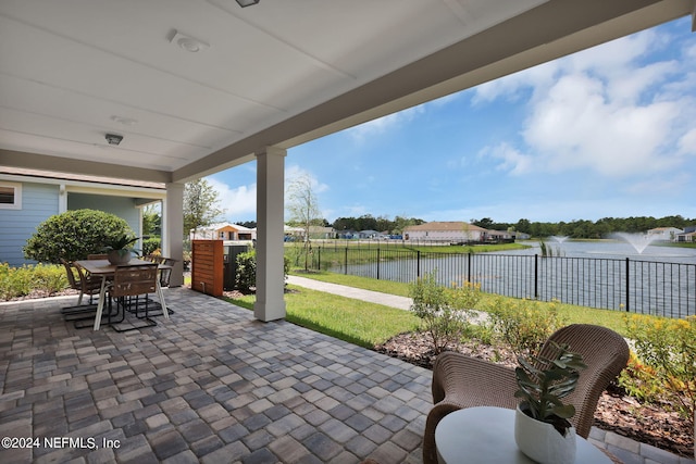 view of patio featuring outdoor dining space, a water view, and fence