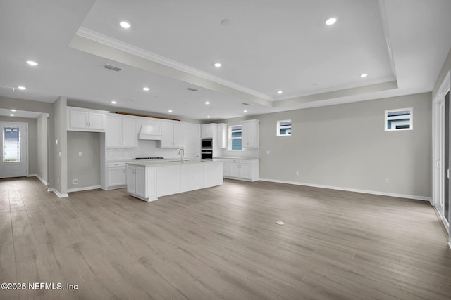 unfurnished living room with light wood finished floors, visible vents, crown molding, a raised ceiling, and a sink