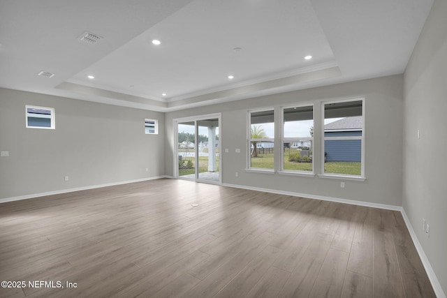 spare room with baseboards, a raised ceiling, and wood finished floors