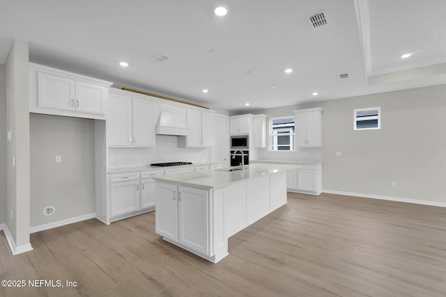 kitchen featuring stainless steel microwave, visible vents, premium range hood, black cooktop, and a sink