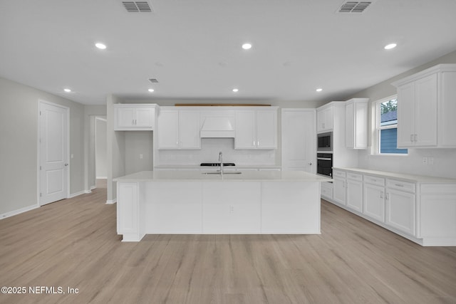 kitchen with light wood finished floors, visible vents, a center island with sink, and stainless steel microwave