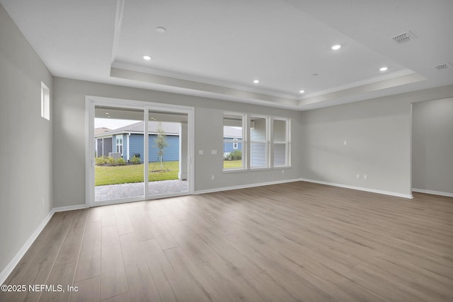 spare room with a tray ceiling, wood finished floors, and visible vents