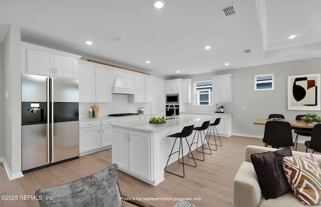 kitchen featuring a sink, stainless steel appliances, a breakfast bar area, white cabinets, and custom exhaust hood