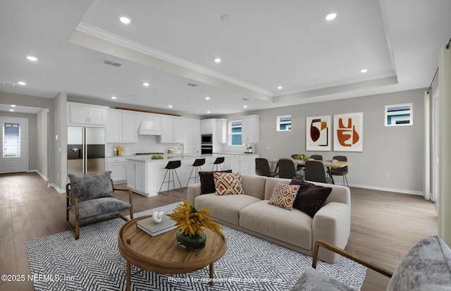 living room with light wood finished floors, visible vents, crown molding, and a raised ceiling