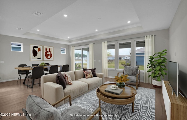 living room featuring visible vents, a raised ceiling, baseboards, and wood finished floors