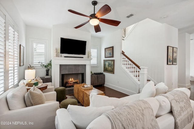 living room with dark wood-type flooring, ceiling fan, a tile fireplace, and a healthy amount of sunlight