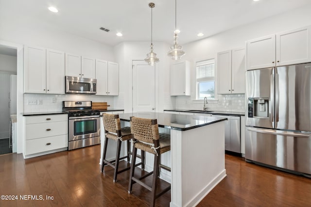 kitchen with dark hardwood / wood-style flooring, white cabinets, sink, a kitchen island, and appliances with stainless steel finishes