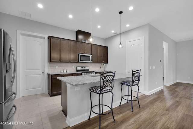 kitchen featuring a kitchen island with sink, hanging light fixtures, sink, light stone countertops, and appliances with stainless steel finishes