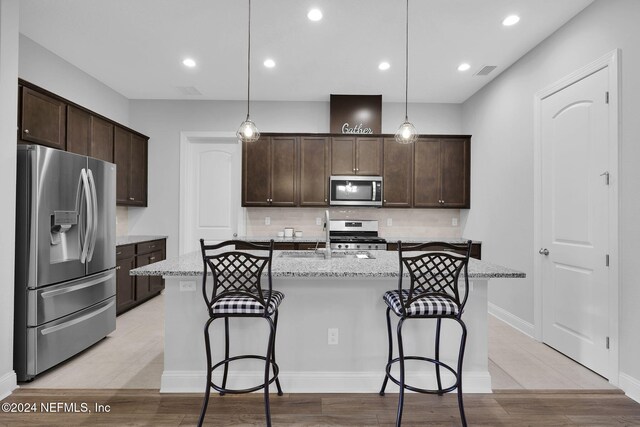 kitchen with a center island with sink, appliances with stainless steel finishes, and hanging light fixtures