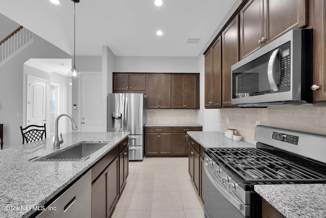 kitchen featuring decorative backsplash, sink, light stone countertops, pendant lighting, and appliances with stainless steel finishes