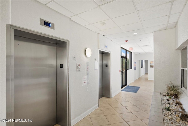 corridor with light tile patterned flooring, elevator, and a paneled ceiling