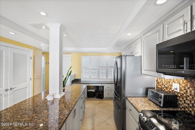 kitchen featuring light tile patterned flooring, dark stone counters, white cabinetry, appliances with stainless steel finishes, and decorative columns