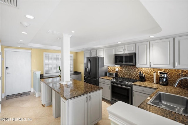 kitchen with decorative columns, appliances with stainless steel finishes, sink, and a tray ceiling