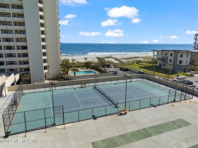 view of tennis court with a water view and a view of the beach