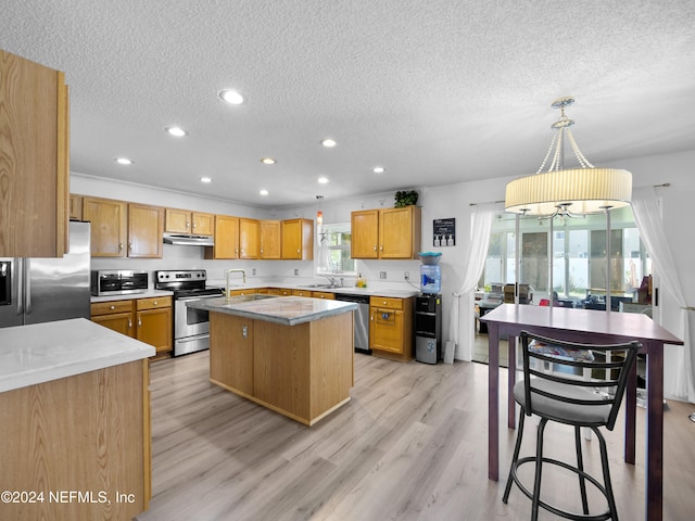 kitchen featuring appliances with stainless steel finishes, sink, a center island, light hardwood / wood-style floors, and decorative light fixtures