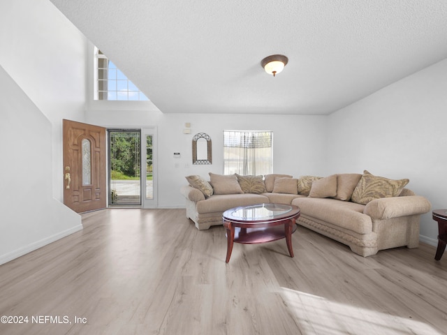 living room featuring a towering ceiling, a textured ceiling, and light wood-type flooring