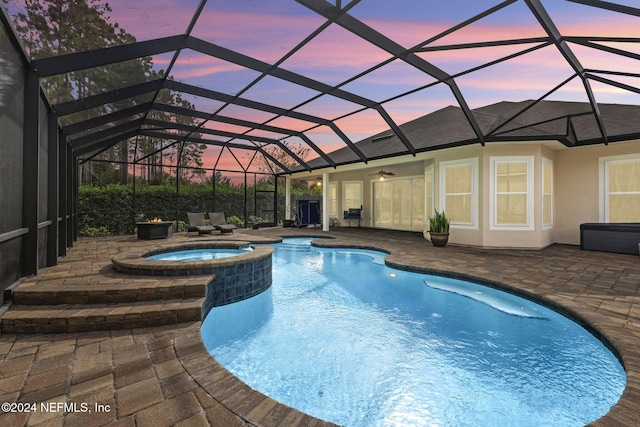 pool at dusk with an in ground hot tub, a patio, and a lanai