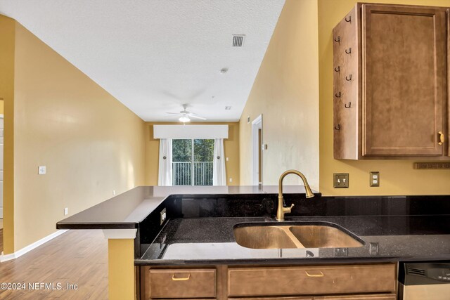 kitchen with dark stone counters, a textured ceiling, sink, vaulted ceiling, and light hardwood / wood-style flooring