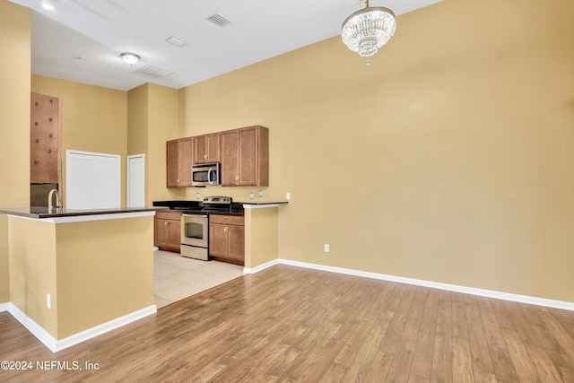 kitchen featuring kitchen peninsula, a chandelier, light wood-type flooring, appliances with stainless steel finishes, and decorative light fixtures