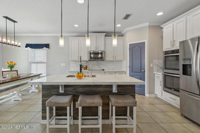 kitchen featuring stainless steel appliances, a center island with sink, crown molding, white cabinetry, and decorative light fixtures