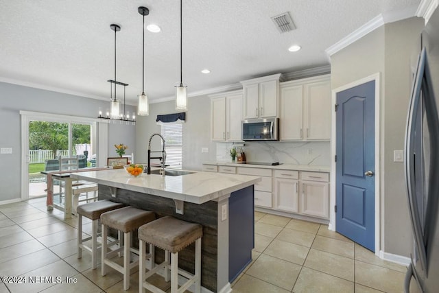 kitchen with stainless steel appliances, white cabinetry, sink, decorative light fixtures, and a kitchen island with sink