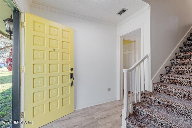 foyer entrance with light hardwood / wood-style flooring, a textured ceiling, and crown molding