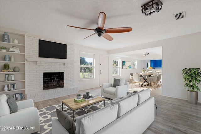 living room featuring built in features, a textured ceiling, hardwood / wood-style flooring, a brick fireplace, and ceiling fan