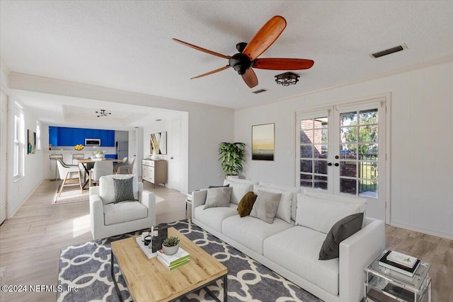 living room with french doors, light wood-type flooring, a textured ceiling, and ceiling fan