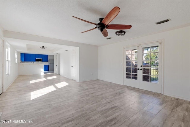 unfurnished living room featuring a textured ceiling, french doors, light hardwood / wood-style flooring, and ceiling fan