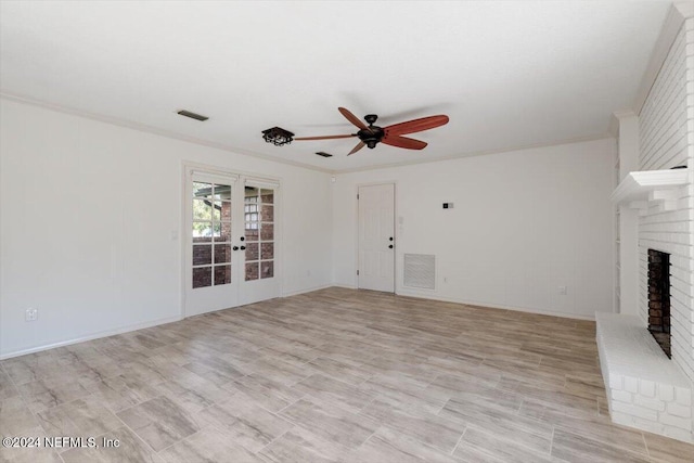 unfurnished living room featuring light hardwood / wood-style floors, ceiling fan, crown molding, a brick fireplace, and french doors