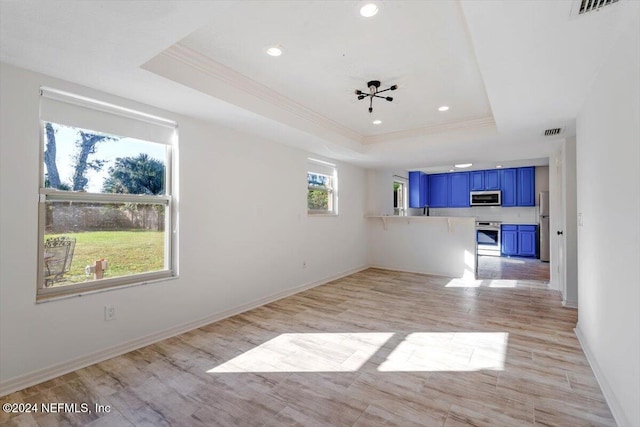 empty room with light wood-type flooring, a tray ceiling, and ornamental molding