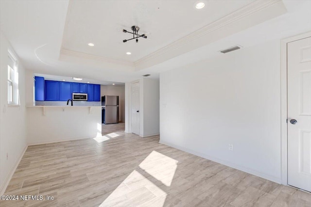 unfurnished living room with light hardwood / wood-style floors, a raised ceiling, and ornamental molding