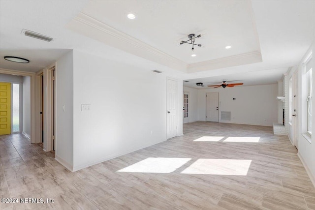 empty room with a tray ceiling, crown molding, ceiling fan, and light hardwood / wood-style flooring