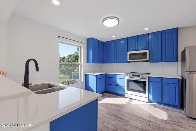 kitchen featuring stainless steel appliances, light hardwood / wood-style floors, blue cabinets, decorative backsplash, and sink