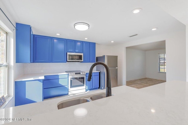 kitchen featuring a wealth of natural light, blue cabinetry, backsplash, and appliances with stainless steel finishes