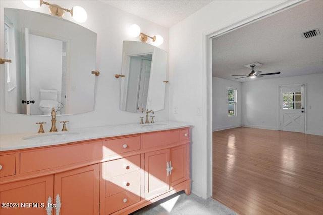 bathroom featuring ceiling fan, a textured ceiling, wood-type flooring, vanity, and toilet