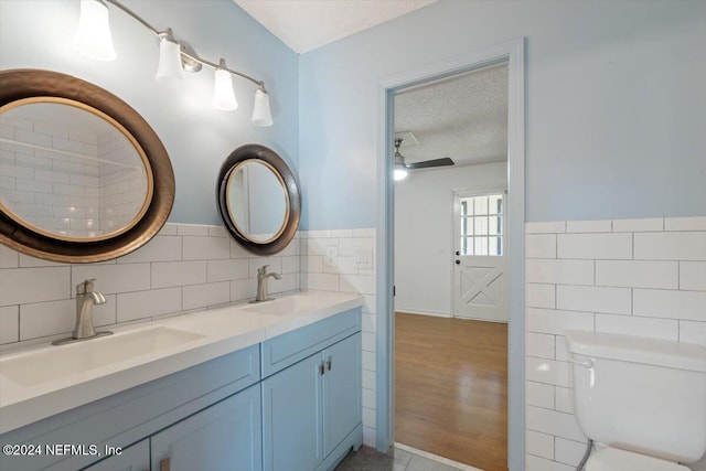 bathroom with a textured ceiling, hardwood / wood-style floors, vanity, toilet, and tile walls