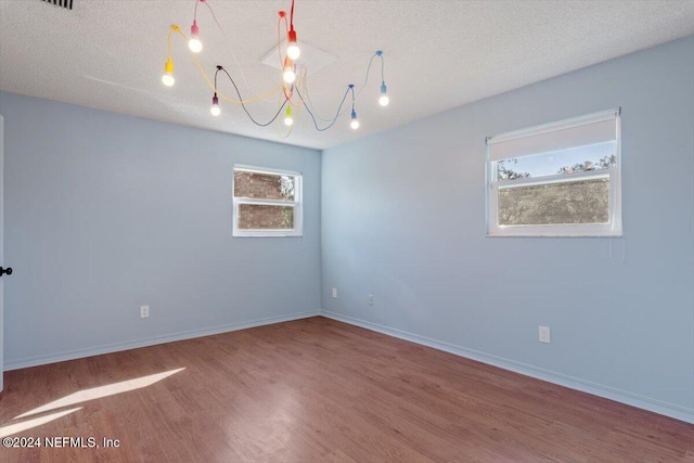 spare room featuring wood-type flooring, a textured ceiling, and an inviting chandelier