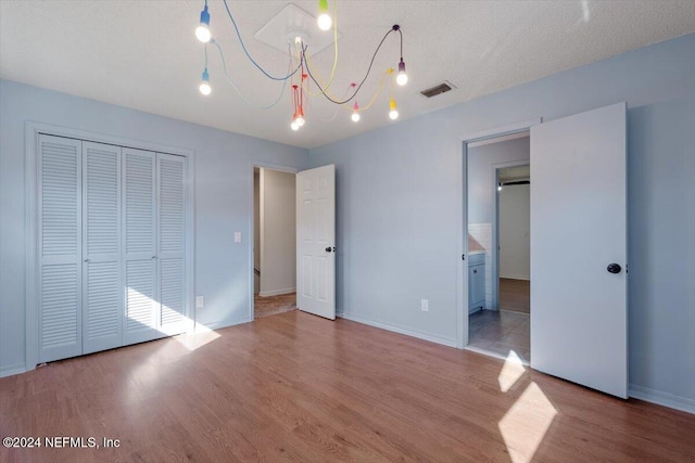 unfurnished bedroom featuring a closet, a textured ceiling, light hardwood / wood-style floors, and ensuite bathroom